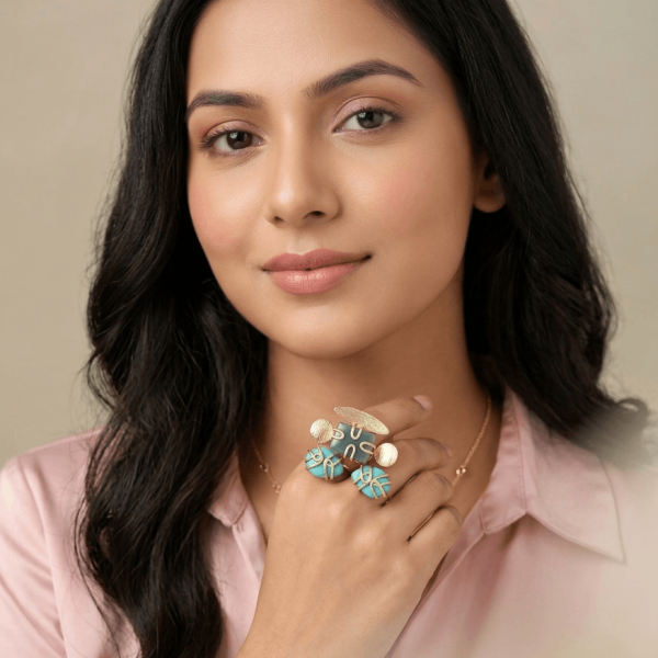 A lifestyle shot of a woman wearing an intricate gold ring with teal amazonite and bright blue caged turquoise gemstones on her hand.