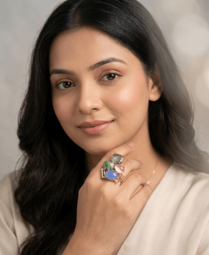 Multi-Stone Architectural Statement Ring – Handcrafted Gold Geometric Cocktail Ring 1 A lifestyle close-up of a woman wearing a large geometric gold ring featuring four different colored gemstones including pink, blue, iridescent grey, and green.