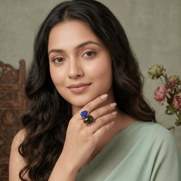A lifestyle shot of a woman in a green saree wearing an intricate gold geometric ring by Belsi's Jewelry featuring a blue lapis lazuli and a large black onyx stone.