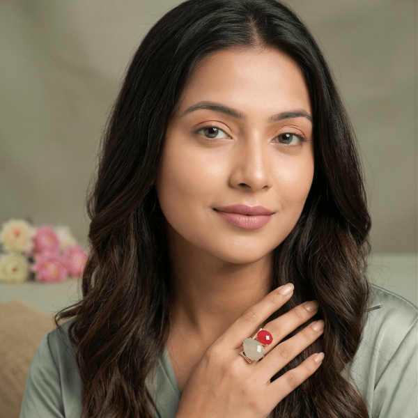 A lifestyle close-up of a woman wearing an intricate gold geometric ring by Belsi's Jewelry featuring a vibrant red faceted stone and a large white moonstone.