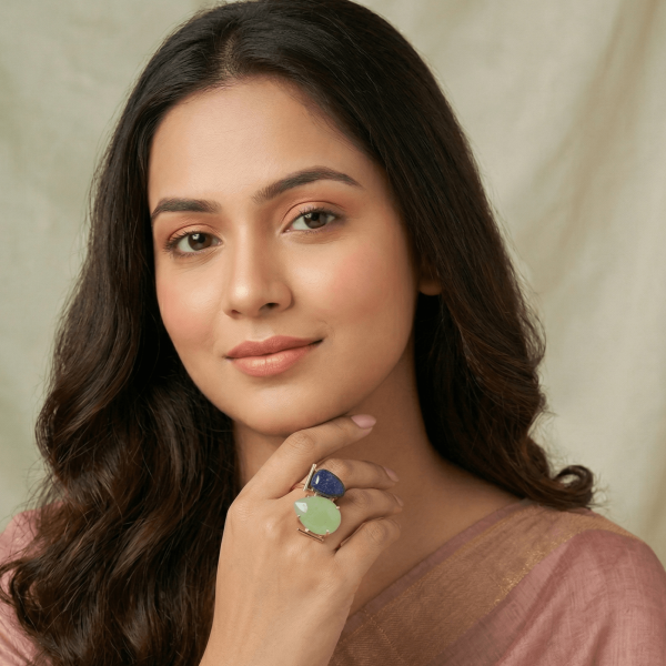 A lifestyle close-up of a woman in a mauve saree wearing an intricate gold geometric ring by Belsi's Jewelry featuring a blue lapis lazuli and a green aventurine stone.