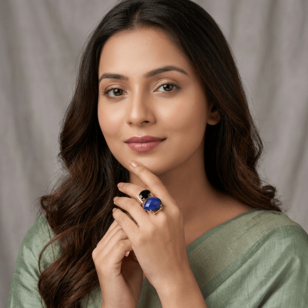 A lifestyle close-up of a woman in a sage green saree wearing an intricate gold geometric ring by Belsi's Jewelry featuring a large blue faceted lapis lazuli and a black onyx.