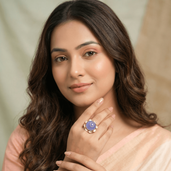A lifestyle shot of a woman in a peach-colored saree wearing a large round gold floral ring with a central blue chalcedony stone.