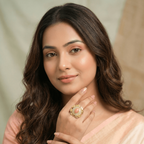 A lifestyle shot of a woman in a peach saree wearing a large round gold floral ring with a tiered white moonstone and peach center stone.