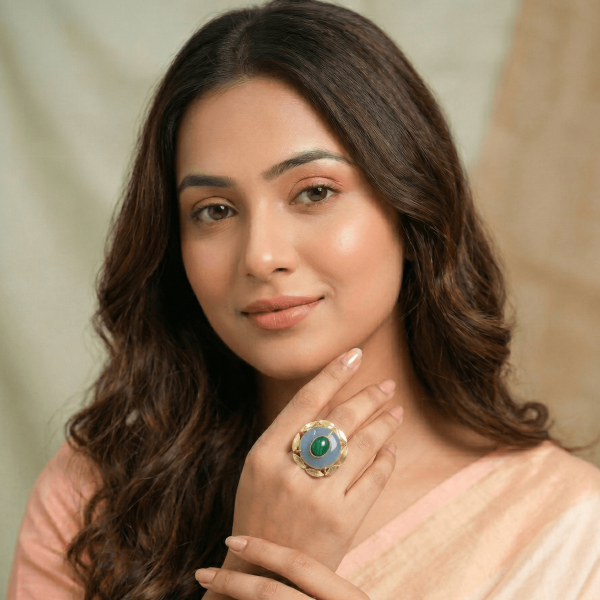 A lifestyle shot of a woman in a peach saree wearing a large round gold floral ring with a tiered blue chalcedony and green malachite center stone.