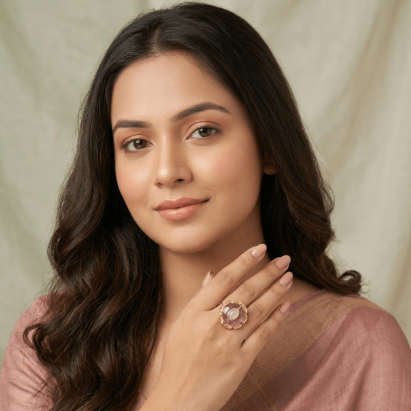 A lifestyle shot of a woman in a mauve saree wearing a large round gold floral ring with a tiered rose quartz and white moonstone center stone.