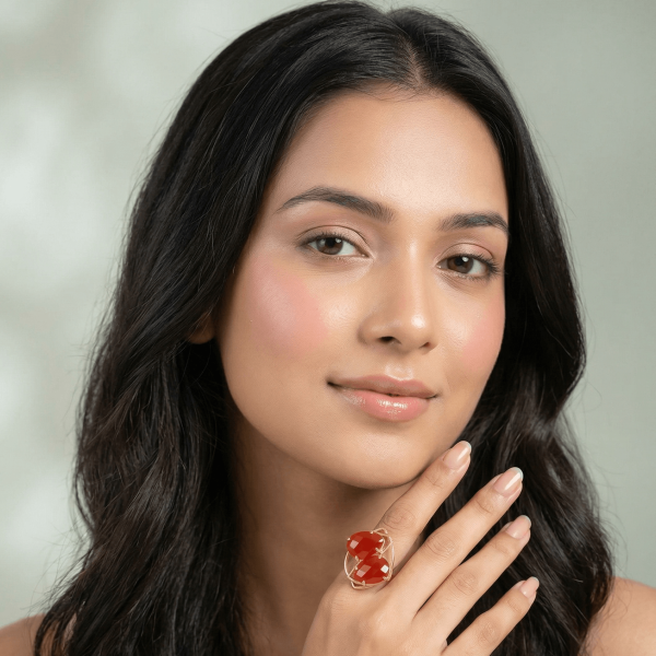 A lifestyle close-up of a woman wearing a modern gold ring by Belsi's Jewelry featuring two interlocking red-orange faceted gemstones.