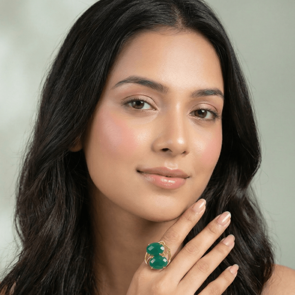 A lifestyle close-up of a woman wearing a modern gold ring by Belsi's Jewelry featuring two interlocking green faceted gemstones.