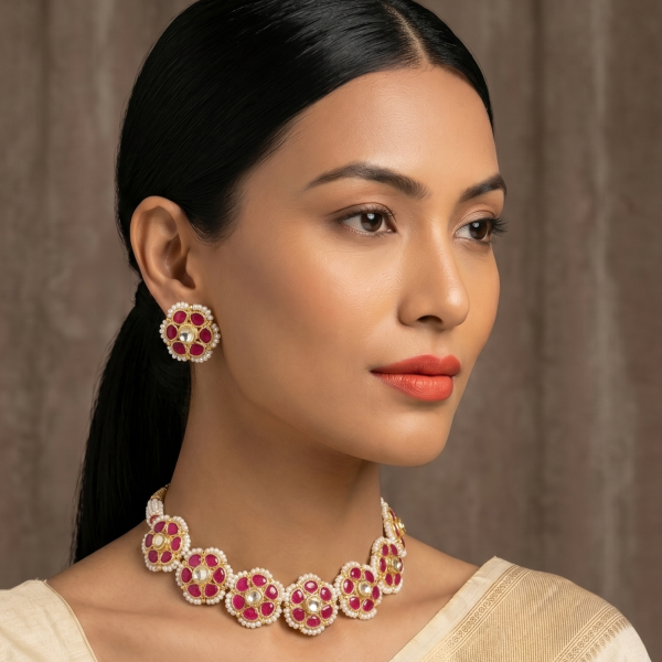 Elegant Indian model in a white and gold saree wearing a ruby-red floral Kundan choker necklace and matching round floral stud earrings.