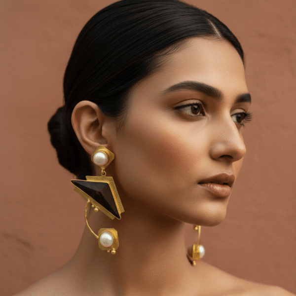 model wearing large, sculptural statement earrings featuring a triangular dark rosewood element, a curved gold-toned bar, and radiant white pearls.