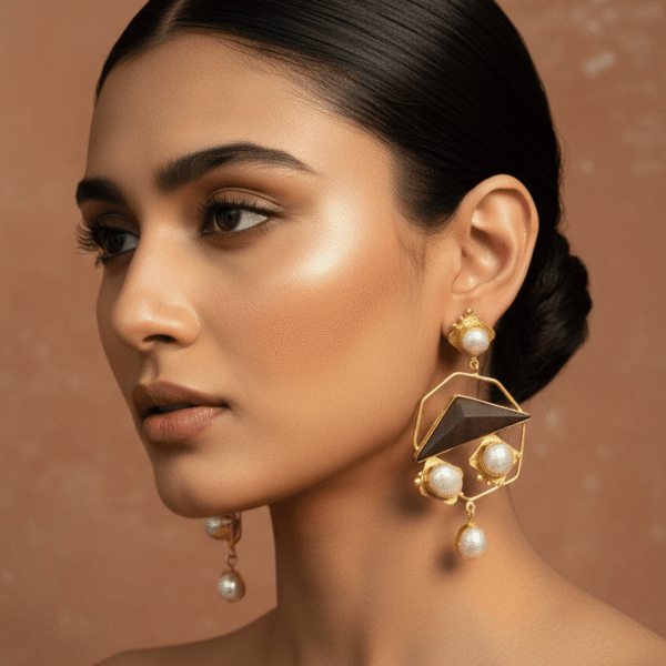 A close-up profile of a woman wearing a large statement earring that features a gold geometric frame, a dark triangular center, and multiple baroque pearls.