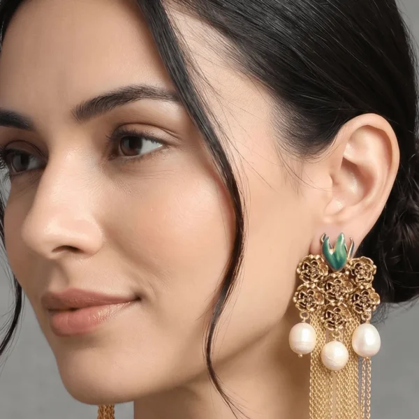 Close-up profile of a model wearing Belsi's Jewelry Flower Power collection gold tassel earrings featuring intricate floral cluster filigree, green enamel detailing, and hanging freshwater pearls with long chain fringes.