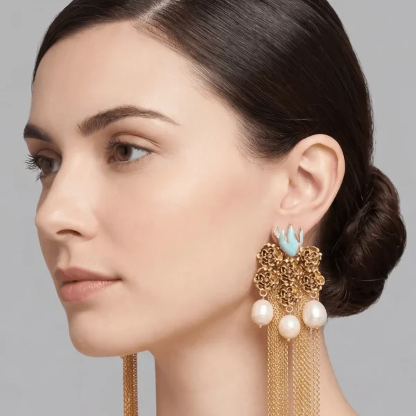 Studio profile portrait of a model showcasing Belsi's Jewelry Flower Power collection long gold tassel earrings featuring intricate textured floral filigree studs, light turquoise blue enamel accents, and three hanging freshwater pearls with fluid chain fringes.