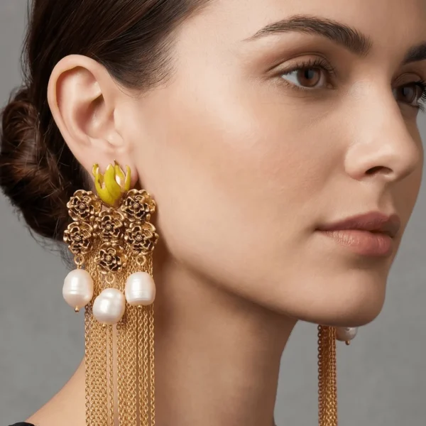 Close-up studio profile portrait of a model showcasing Belsi's Jewelry Flower Power collection long gold tassel earrings, designed with a textured floral cluster stud, vibrant lime yellow enamel accents, and hanging freshwater pearls with fluid gold chain fringes.