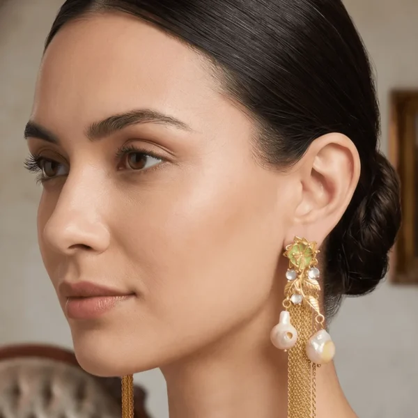 Studio profile portrait of a model showcasing Belsi's Jewelry Flower Power collection long statement earrings, featuring a pastel mint green enamel top flower, a gold leaf vine drop structure accented with clear stones, and two hanging baroque pearls with ultra-fine gold chain fringes.
