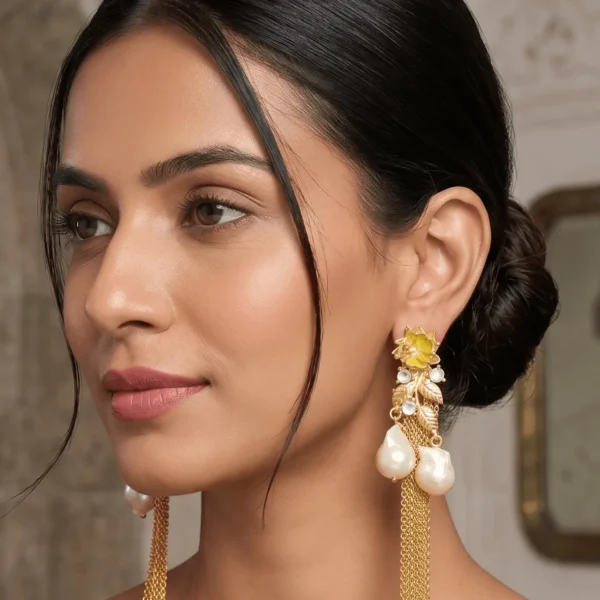 Studio product shot against a gray background showcasing a pair of Belsi's Jewelry Flower Power collection long statement earrings, featuring a citrusy lime yellow enamel top flower, a textured gold leaf vine body with round clear crystal inserts, and two large hanging baroque pearls with fluid gold chain tassels.