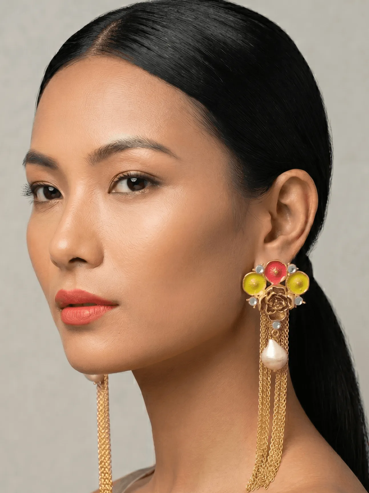 Flower Power Gold Geometric Fan Tassel Earrings with Coral Red & Lime Yellow Enamel 1 Close-up portrait of a model showcasing Belsi's Jewelry Flower Power collection long statement earrings, featuring a golden rose stud topped with a fan of hand-painted coral red and vibrant lime yellow enamel circles, clear stone borders, a central hanging drop pearl, and long gold chain fringe tassels.