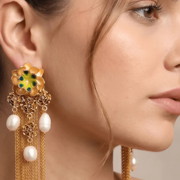 Extreme close-up portrait of a model showcasing Belsi's Jewelry Flower Power collection long statement earrings, featuring a large tiered gold flower stud with hand-painted lime yellow-green and deep peacock green enamel petals, a cluster drop of smaller filigree roses, hanging baroque freshwater pearls, and long fluid gold chain fringe tassels.