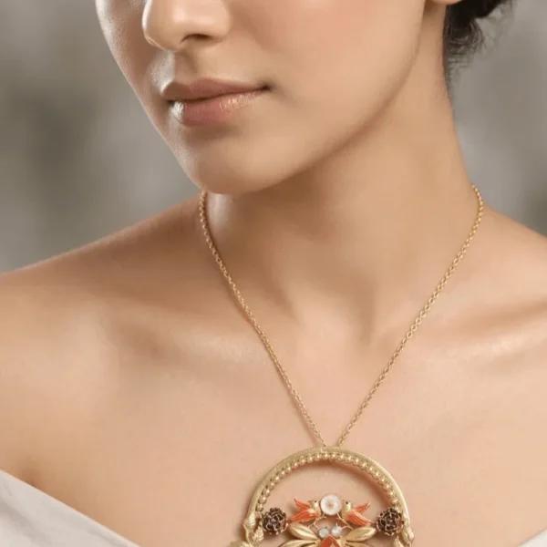 A close-up studio photograph of a fashion model with a long neck and sleek tied-back hair wearing a large, circular gold statement pendant necklace detailed with artisan birds and floral motifs.