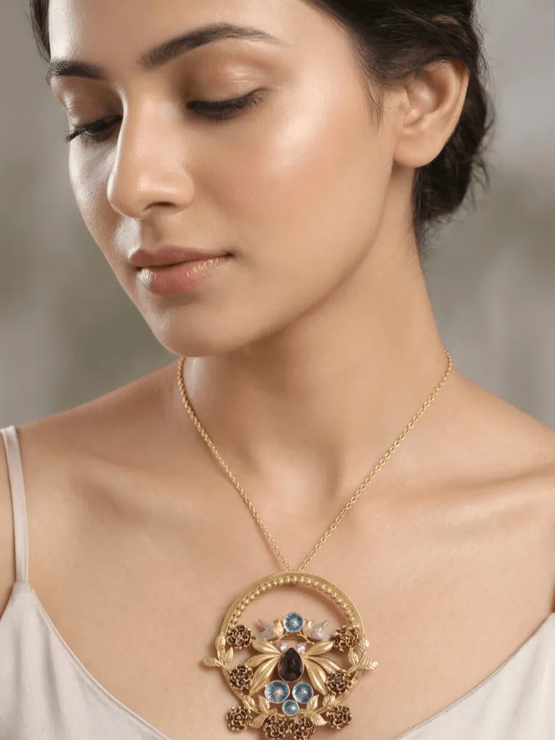 The Mayurika Handcrafted Gold & Peacock Blue Statement Pendant 1 A high-fashion editorial close-up of a model wearing a large circular gold statement pendant with handcrafted leaves, peacock blue floral rosettes, and a dark central gemstone.