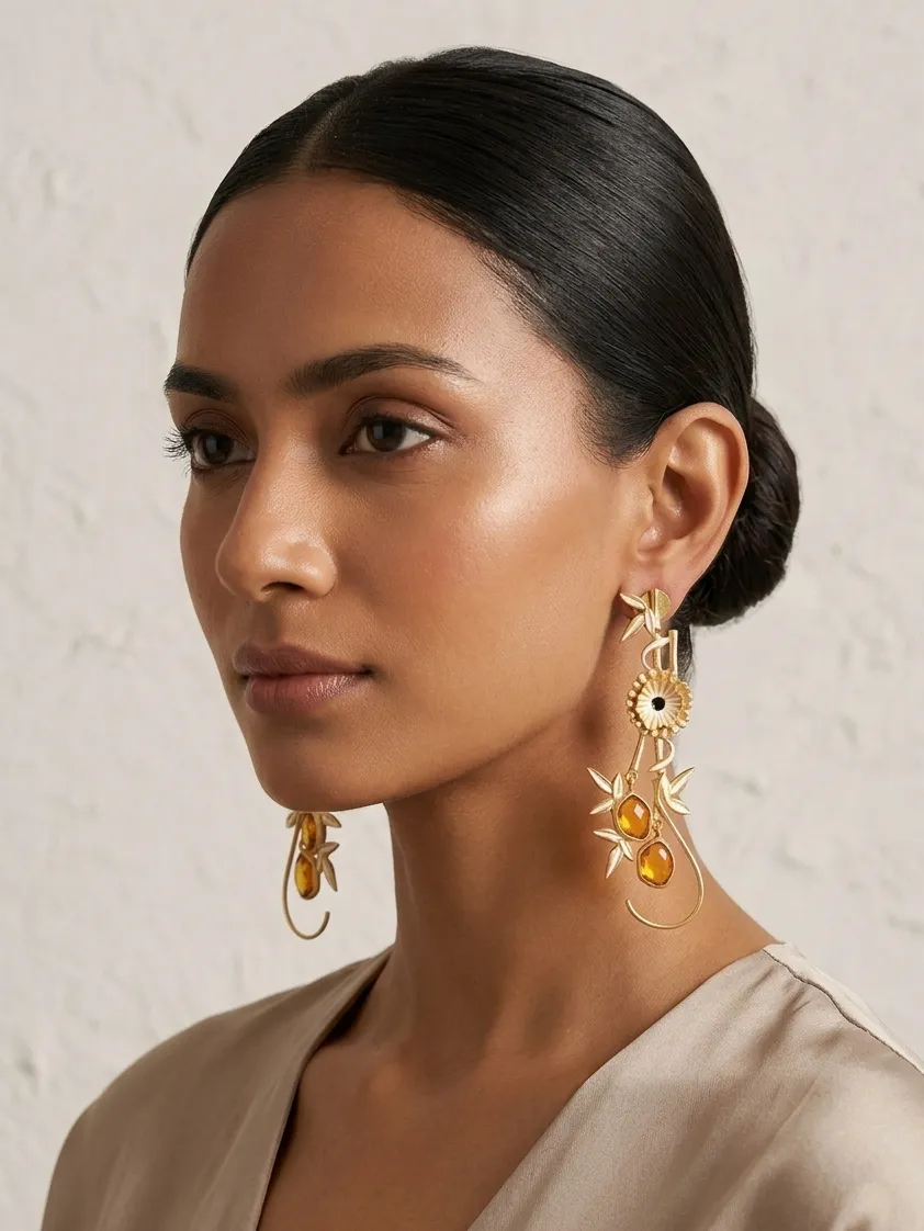 Aura Bamboo & Floral Drop Earrings in Gold-Tone with Amber Gemstones 1 Model wearing long gold-tone statement drop earrings featuring polished gold bamboo accents, a central floral motif, and warm honey-amber oval gemstones on a delicate wire loop.