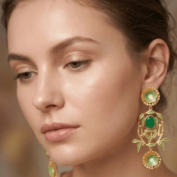 Close-up of a model wearing large, ornate gold-tone chandelier statement earrings featuring dual pastel green enamel floral disks, a central framing bamboo arch, and a vibrant jade green oval cabochon stone.