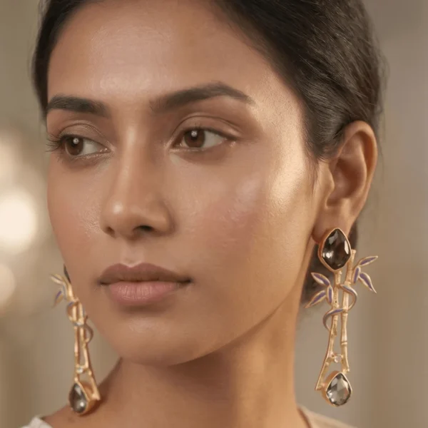 A pair of gold-tone statement earrings shaped like textured bamboo branches, featuring slate grey enamel leaf inlays, subtle crystal accents, and faceted smoky slate grey gemstones.