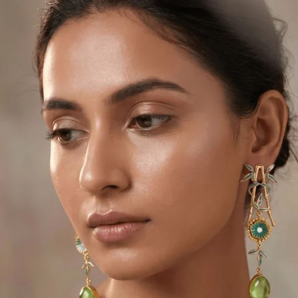 Close-up of a model wearing long gold-tone linear statement earrings featuring periwinkle teal-blue and off-white enamel accents on an architectural bamboo frame, a central fluted floral medallion, and a faceted lime green teardrop gemstone dangling at the base.