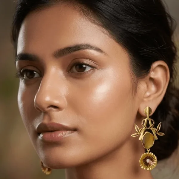 Studio shot of a pair of gold-tone statement drop earrings featuring a linear post, an openwork bamboo branch frame forming a shield silhouette with dark brown enamel accents, a central smooth oval translucent yellowish-brown honey gemstone, and a tiered fluted medallion filled with enamel work at the base.