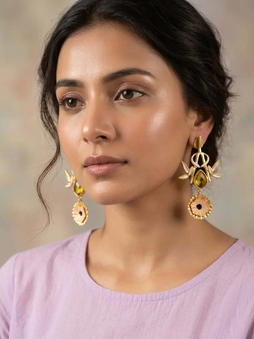 Essence Enamelled Bamboo Shield Drop Earrings with Olive Green Gemstones & Peach Accents 1 Close-up of a model wearing gold-tone statement drop earrings featuring a linear post, an openwork bamboo frame forming a shield silhouette with soft peach-cream enamel accents, a central faceted teardrop olive-green gemstone, and a tiered fluted peach medallion dangling at the base.