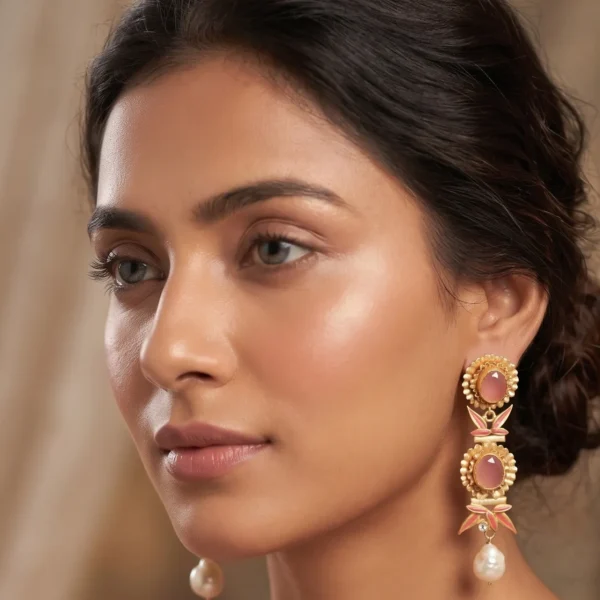 Close-up of a model wearing gold-tone linear statement earrings featuring a tiered arrangement of two fluted concentric medallions set with translucent soft pink stones, separated by peach pink enamel bamboo leaves and crystal nodes, finished with a dangling organic baroque pearl.